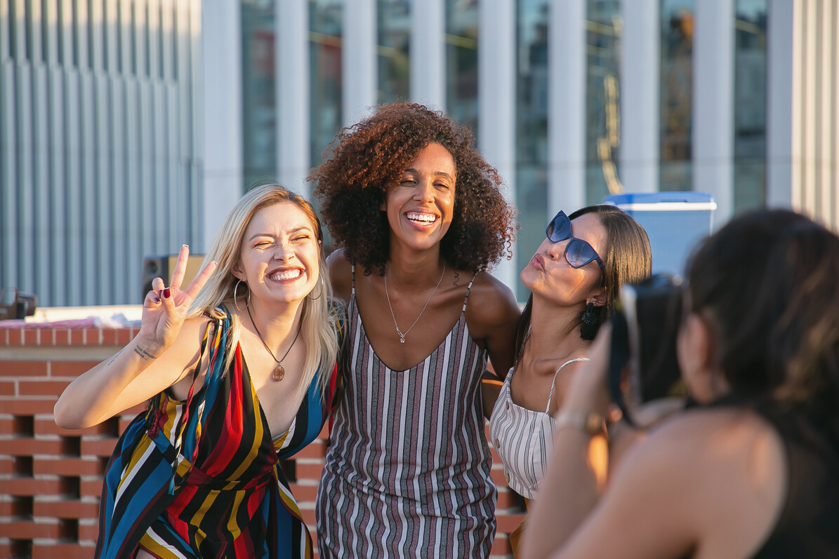 Anonymous woman photographing positive diverse ladies during event on rooftop